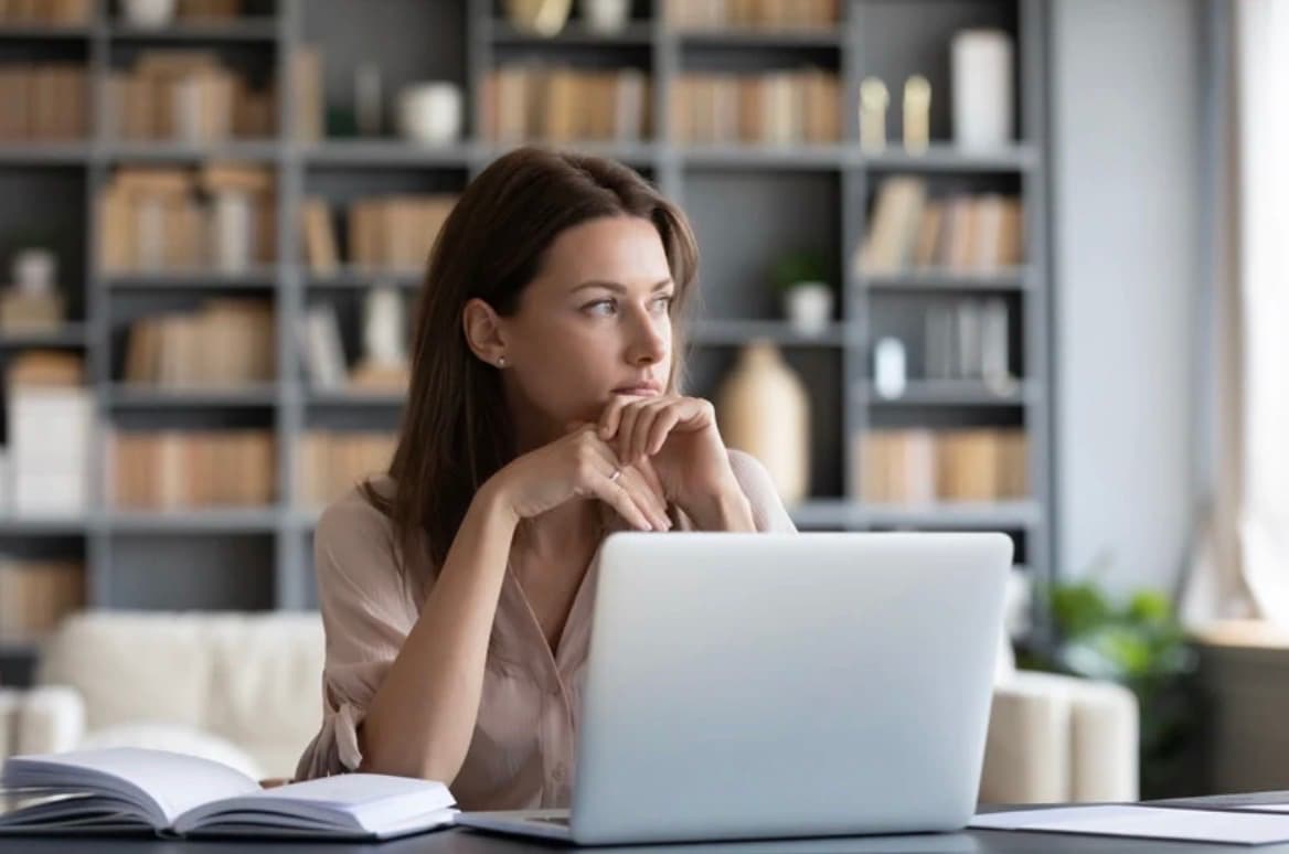 Woman sitting with an open laptop, hesitating before starting something new
