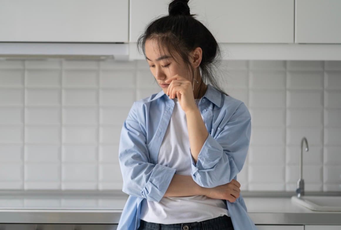Woman in her kitchen looking down, carrying the quiet weight of high-functioning anxiety